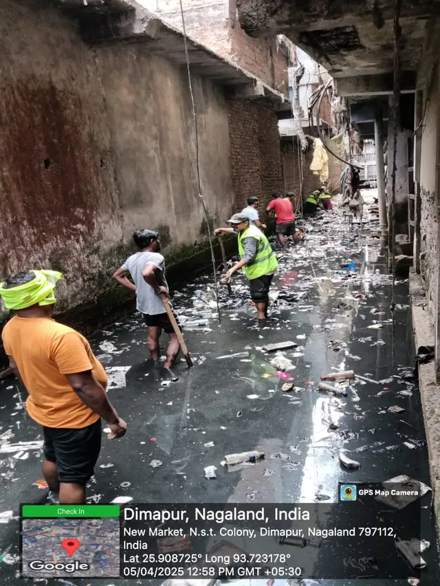 Workers cleaning a narrow drain between buildings